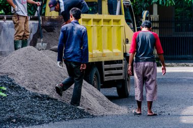 İnşaat alanı inşaatı için kamyondan kumları atan ve taşları kürekle kıran insanlar.