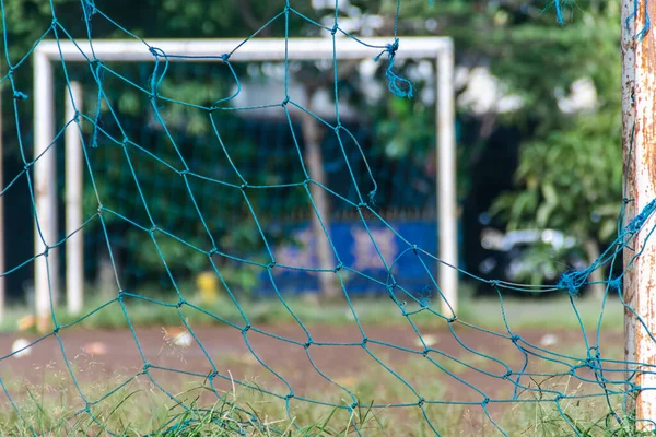 teared blue mesh of foot ball or soccer goal post with blurry field background