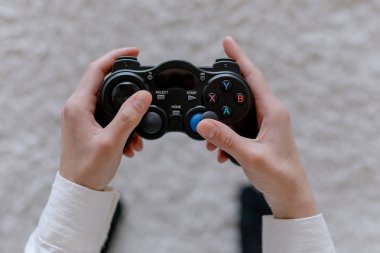 Kadın elleri oyun konsolundan bir joystick tutuyor.