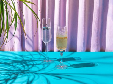İçinde köpüklü içecekler ve yanında tropikal yapraklar bulunan eşsiz, lüks kristal bardaklar. Parti konseptinden sonra karamsar gölge, zambak ipeği ve mavi arka plan.