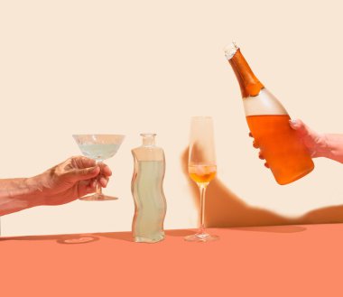 Çeşitlilik partisi konsepti. Erkek eli, içinde içki olan antika bardakları tutuyor ve kızlar şampanya şişesini tutuyor. Güzel kıvrımlı bardaklar, bej ve terracotta arka planlarına karşı körüklüyor.