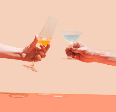 İki el, bir adam eşsiz bir bardak tutuyor ve kızın elinde bej ve terracotta arka planında güzel kırmızı içkiler olan lüks bir kristal bardak var. Yıldönümü kutlaması kavramı.