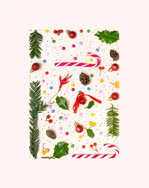 Awesome winter party frame inspired concept. Beautiful christmas pattern made of candy canes, pine cone, pine branches, red berries, colorful sugar coated round chocolate balls. Beige background