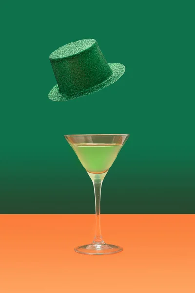 アイルランドの祭りの最小コンセプト テラコッタのテーブルの上に緑のカクテルとマルティーニグラス 濃い緑色の背景の上に浮かぶ緑の輝きの帽子 — ストック写真
