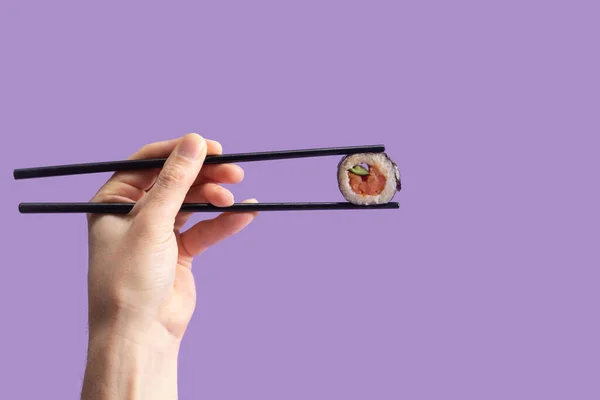 Sushi eating minimal concept. Man hand holding black chopstick with one piece rice salmon and cucumber roll in nori dried edible seaweed. Veri peri background
