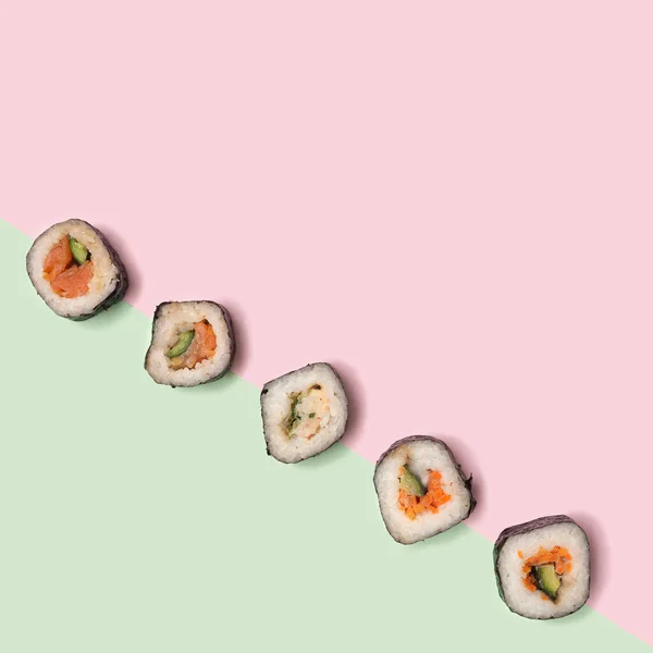 Flat lay sushi vegetarian concept. Many sushi with salmon, squid, tuna fish, rice, cucumber carrots  and nori seaweed rolls are diagonal on pastel pink and green background. Creative copy space above.