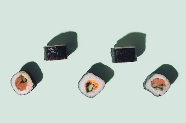 Vegetarian flat lay sushi concept. Many sushi with salmon, squid, tuna fish, rice, cucumber carrots  and nori seaweed rolls on pastel green background.