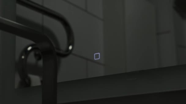A kéz ki és bekapcsolja az érintőlámpát kapcsolja be a háttérvilágítást a zuhany alatt a fürdőszobai tükörben közelkép — Stock videók