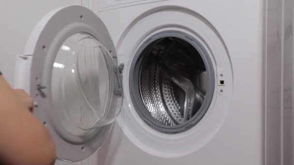 Uma mulher coloca coisas na máquina de lavar roupa, uma menina na lavanderia, close-up — Vídeo de Stock