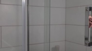 Bir kadın eli duş kabininin cam kapısını açar, şeffaf duvar, yakın plan.