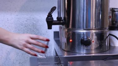 Bir kadın eli musluğu açar ve sıcak suyu bardağa çevirir, kaynar su, demleme içecekleri.