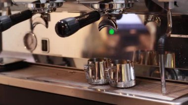 Mutfaktaki barista kahve makinesini çalıştırıyor, kahve bardaklara doluyor.