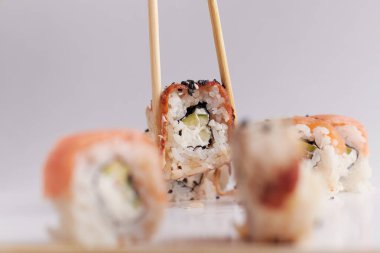 Bir el ve Çin yemek çubukları diğer suşilerin üzerinde bir rulo tutar, Asya yemeğinin bir kısmı, rulo yapar.