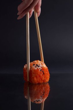 Bir el ve Çin yemek çubukları diğer suşilerin üzerinde bir rulo tutar, Asya yemeğinin bir kısmı, rulo yapar.