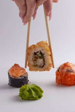 Bir el ve Çin yemek çubukları diğer suşilerin üzerinde bir rulo tutar, Asya yemeğinin bir kısmı, rulo yapar.