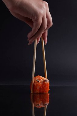 Bir el ve Çin yemek çubukları diğer suşilerin üzerinde bir rulo tutar, Asya yemeğinin bir kısmı, rulo yapar.