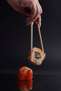 Bir el ve Çin yemek çubukları diğer suşilerin üzerinde bir rulo tutar, Asya yemeğinin bir kısmı, rulo yapar.