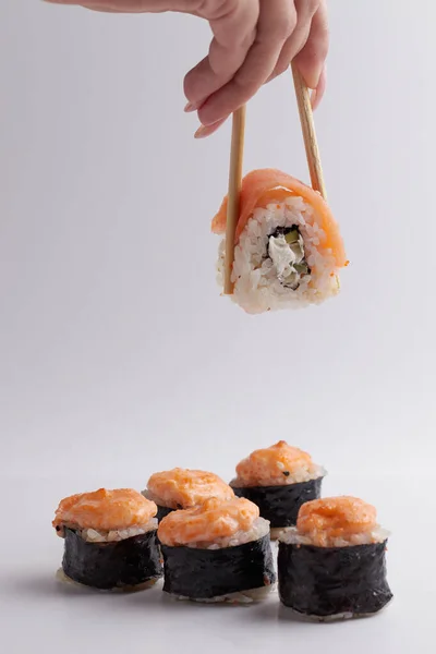 Ruka a čínské hůlky drží roli přes jiné sushi, porce asijského jídla, rolky — Stock fotografie