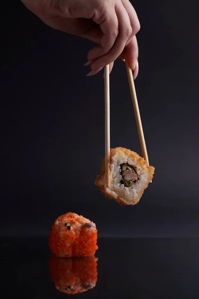 Una mano y palillos chinos sostiene un rollo sobre otro sushi, una porción de comida asiática, rollos — Foto de Stock