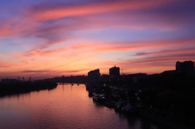 Şehirde gün batımı, güneş ışınları, altın saat, su ve gemiler, akşam manzarası.