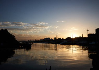 Şehirde gün batımı, güneş ışınları, altın saat, su ve gemiler, akşam manzarası.