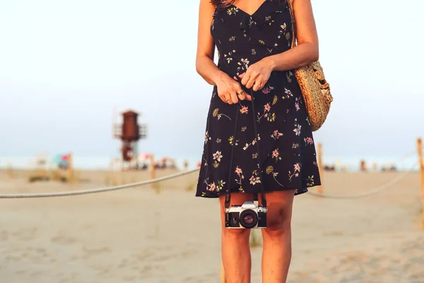 Young woman walking with an analog camera on the beach