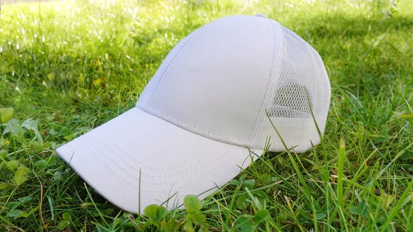 Fehér baseball sapka gúnyolódik a padon. Fénykép üres kalap a változás design. A zöld füvön történő márkaépítés eleme — Stock Fotó