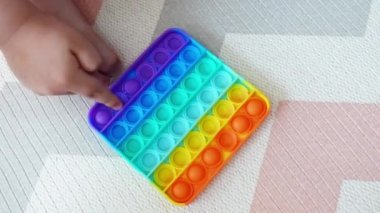 Stres önleyici pop-it oyuncağı. Gökkuşağı duyusal oyunuyla oynayan çocukların yakın çekimi. Renkli silikon patlat onu oyuncak. Üst Manzara. Popo kabarcığına bas 