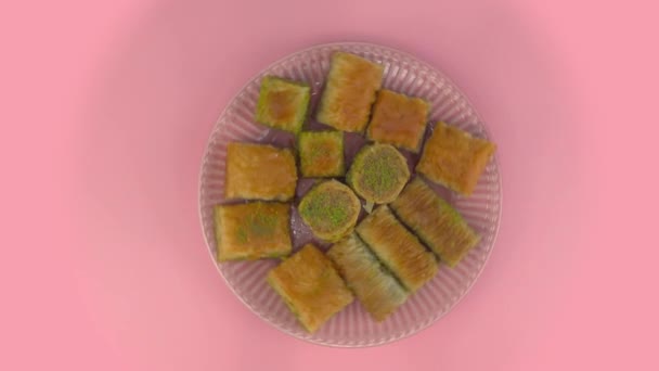 Döner tabakta baklava. Pembe arka planda oryantal şekerli bir tabak. Doğulu ballı hamur işleriyle dolu bir tabağın üst görüntüsü — Stok video