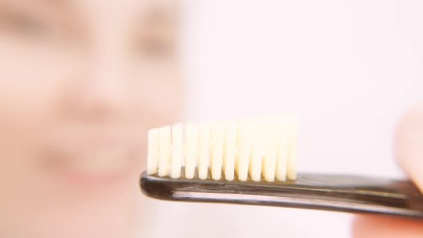 Cepillo de dientes de cerca extremo con hembra europea en el fondo. Fondo borroso de la cara. Chica aplicando pasta de dientes blanca a su cepillo de dientes — Vídeos de Stock