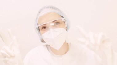 Genç bir doktor salgının sonunda seviniyor. Elleriyle dans eden bir kızın portresi. Gözlüklü bir kadın, beyaz bir solunum cihazı koruyucu eldivenler ve tıbbi bir elbise. Kız gülümsüyor.