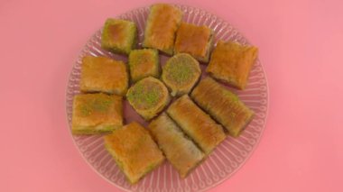 Doğulu tatlıya zum yapıyor. Pembe arka planda oryantal şekerli bir tabak. Doğulu ballı hamur işleriyle dolu bir tabağın üst görüntüsü