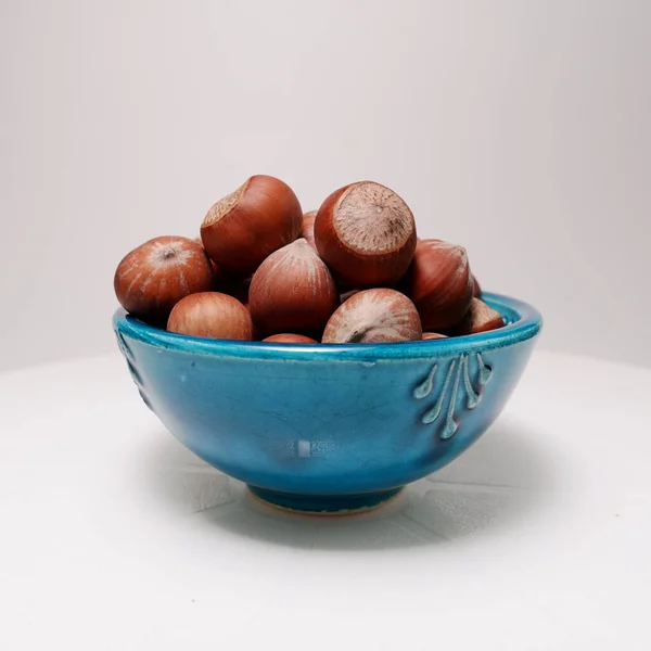 白色背景上陶瓷蓝色碗中的褐色榛子 未剥落的坚果 — 图库照片