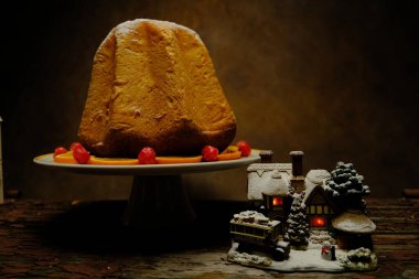 Karlı ve ışıklı bir Noel evi seramik bir arka planda pandoronun yanında.