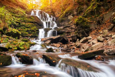 Beautiful waterfall with trees, red leaves, rocks and stones in autumn forest