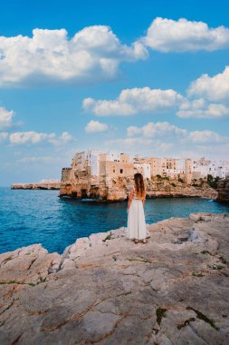 Polignano a Mare, İtalya - Ağustos 2021: Polignano a Mare köyünün önündeki genç kız, gökyüzü beyaz bulutlu