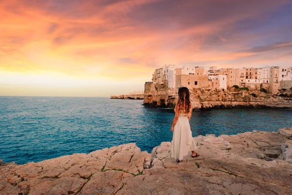 Polignano a Mare, İtalya - Ağustos 2021: Polignano a Mare köyünün önünde gün batımını izleyen genç kız