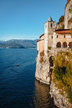 Leggiuno, Varese, İtalya - Aralık 2021: Santa Caterina del Sasso Hermitage, Maggiore Gölü üzerinde gün batımında tekne ile
