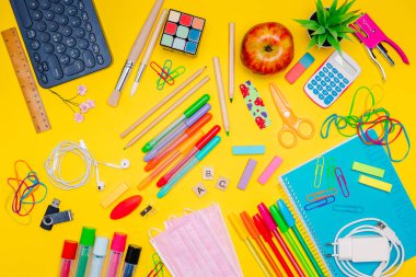 Milan, İtalya - Ocak 2022: Çocuklar için kırtasiye malzemeleri, renkli kalemler, etiketler, ataçlar, sarı arka planda maskeler, okula dönüş konsepti, düz yatış