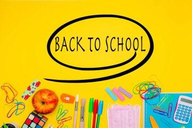 Milan, İtalya - Ocak 2022: Kırtasiye ürünleri, renkli kalemler, etiketler, ataçlar, maskeler ve daha fazlası sarı arka planda, okul harfleri, konsept, düz konum