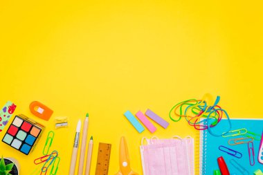 Milan, İtalya - Ocak 2022: Kırtasiye ürünleri, renkli kalemler, etiketler, ataçlar, hesap makineleri, yüz maskeleri ve daha aşağıdaki sarı arka plan, okula dönüş konsepti, düz yer, boş alan
