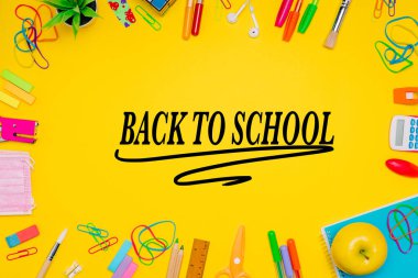 Milan, İtalya - Ocak 2022: Sarı arkaplan, renkli kalemler, etiketler, ataçlar, hesap makinesi, yüz maskesi ve daha fazlası üzerinde sıralanmış kırtasiye ürünleri serisi, merkeze geri döndü, düz yatıyordu