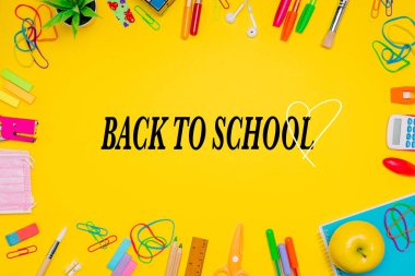 Milan, İtalya - Ocak 2022: Sarı arkaplan, renkli kalemler, etiketler, ataçlar, hesap makinesi, yüz maskesi ve daha fazlası üzerinde sıralanmış kırtasiye ürünleri serisi, merkeze geri döndü, düz yatıyordu