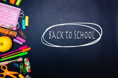 Milan, İtalya - Ocak 2022: Kırtasiye ürünleri, renkli kalemler, etiketler, ataçlar, hesap makinesi, makas, pembe yüz maskeleri ve daha çok siyah arkaplanın sol tarafına yerleştirilmiş olanlar, okula merkezde, düzlükte, konsept içinde geri dönenler