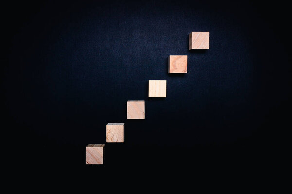 Milan, Italy - January 2022: Series of wooden cubes on black background to fill, empty space, concept of success and idea