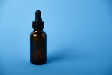 Kehribar damlası şişesinde serum yağı var. Mavi arka planda pipeti olan serum camı şişesi..