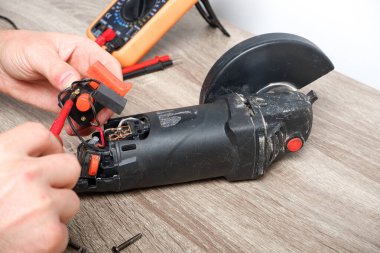 Elektrikli alet tamiri. Bir adam açı öğütücüsünü tamir eder. Tornavida, çoklu metre.