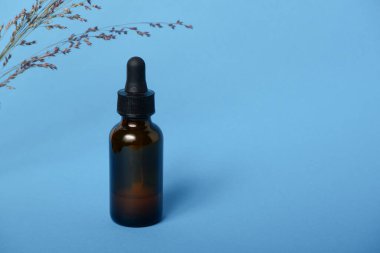 Kehribar damlası şişesinde serum yağı var. Mavi arka planda pipeti olan serum camı şişesi..