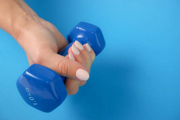 健康的概念一只女性的手握住一个蓝色塑料哑铃 蓝色背景 — 图库照片