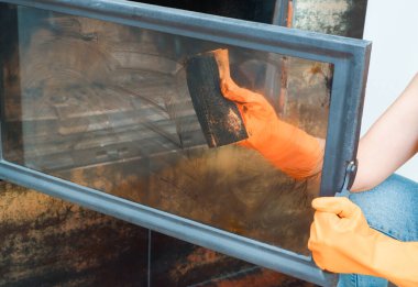 Şömineyi temizliyorum. Turuncu lastik eldivenli kadın elleri şöminenin ısıya dayanıklı camlarını yıkıyor..